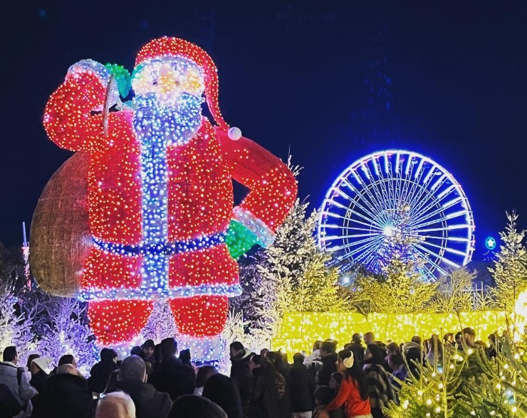 Figura luminosa gigante de Papá Noel junto a una noria iluminada en el Village de Noël de Barcarès.