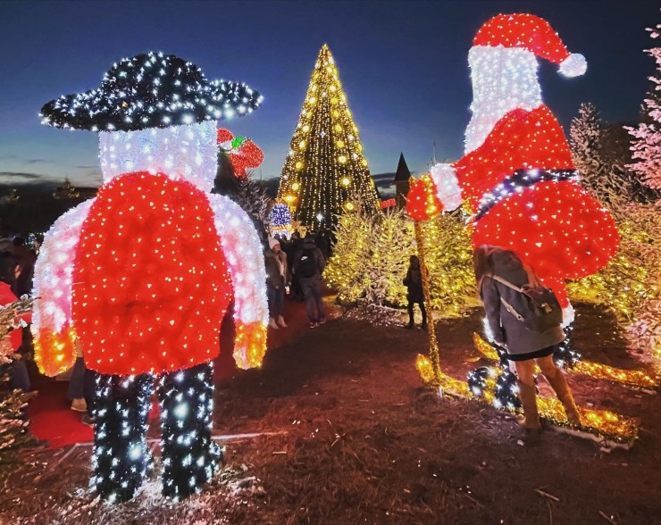 Dos figuras luminosas de Papá Noel y un árbol de Navidad iluminado en un recinto navideño.