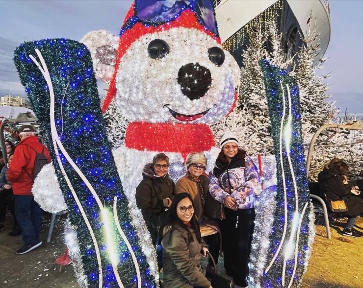 Grupo de personas posando junto a una figura luminosa de un oso con gorro navideño.
